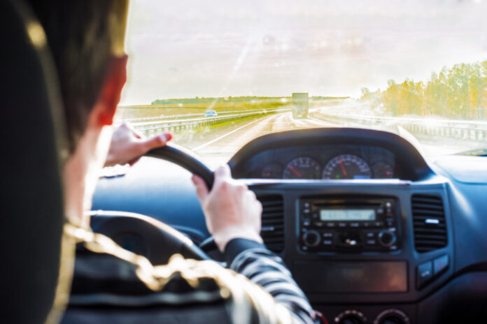Man hand driving a car at sunset evening sky light Autumn Road b